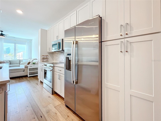 kitchen with light wood finished floors, decorative backsplash, open floor plan, stainless steel appliances, and white cabinetry