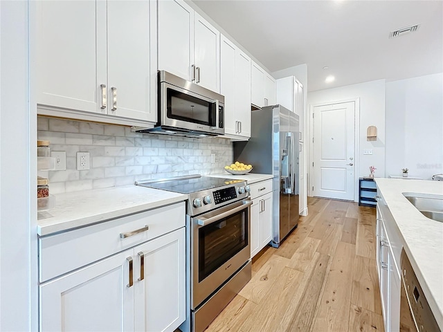 kitchen with tasteful backsplash, visible vents, light wood-style flooring, appliances with stainless steel finishes, and white cabinets