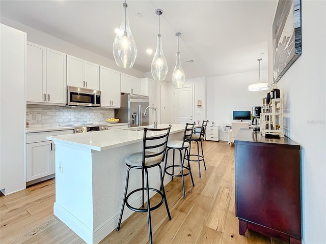 kitchen featuring an island with sink, light wood-style floors, stainless steel appliances, and a sink