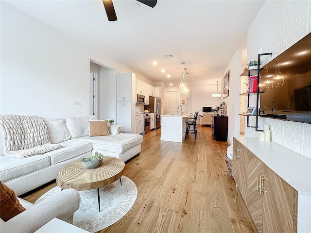 living room with light wood-style floors, visible vents, and a ceiling fan