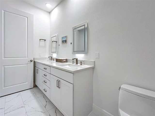 bathroom with toilet, marble finish floor, double vanity, and a sink