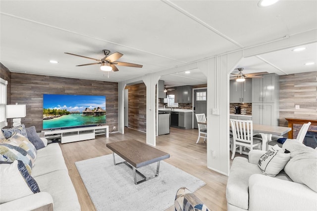 living room featuring light wood-type flooring, ceiling fan, and wood walls