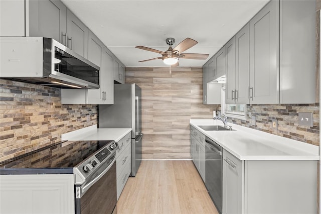 kitchen with gray cabinetry, ceiling fan, sink, stainless steel appliances, and light hardwood / wood-style flooring