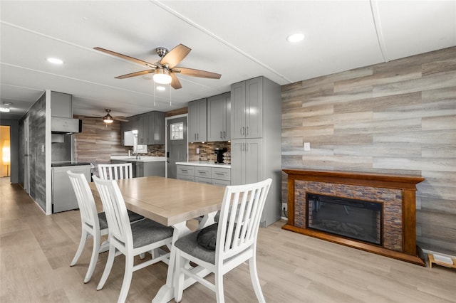 dining room featuring a fireplace, light wood-type flooring, ceiling fan, and sink