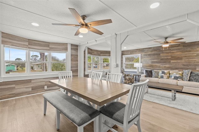 dining space with a textured ceiling, light hardwood / wood-style floors, ceiling fan, and wooden walls