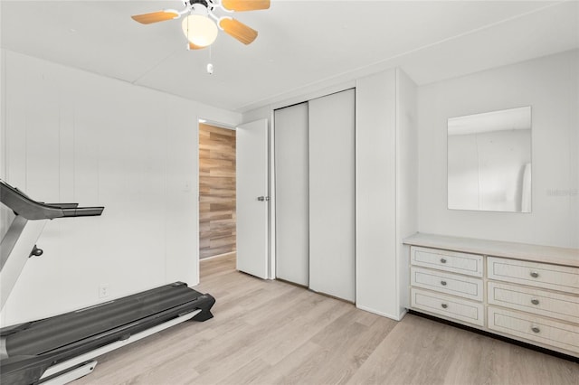 exercise room featuring light hardwood / wood-style flooring, ceiling fan, and wooden walls