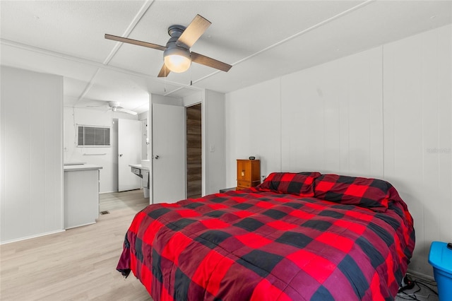 bedroom with ceiling fan, light wood-type flooring, a wall unit AC, and ensuite bath