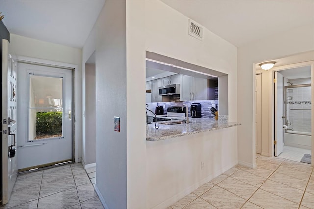 kitchen featuring light stone countertops, light tile patterned floors, decorative backsplash, electric range, and sink