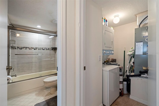 bathroom with stacked washing maching and dryer, toilet, enclosed tub / shower combo, tile patterned floors, and a textured ceiling