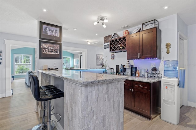 kitchen featuring a breakfast bar area, light hardwood / wood-style flooring, light stone counters, a textured ceiling, and kitchen peninsula