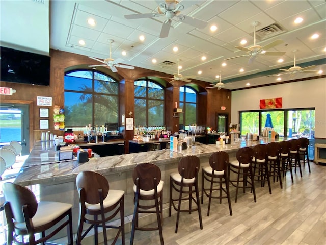 bar featuring a high ceiling, stone counters, and light hardwood / wood-style flooring