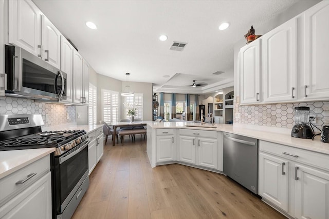 kitchen featuring kitchen peninsula, tasteful backsplash, stainless steel appliances, pendant lighting, and white cabinets