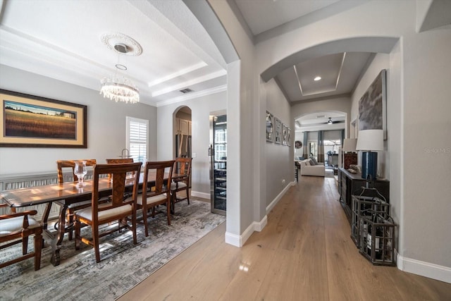 dining space featuring a tray ceiling, wood-type flooring, ceiling fan with notable chandelier, and ornamental molding