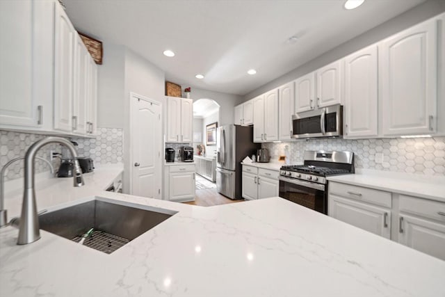 kitchen with light stone countertops, stainless steel appliances, white cabinetry, and sink