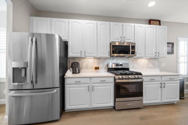 kitchen with tasteful backsplash, light hardwood / wood-style flooring, white cabinets, and appliances with stainless steel finishes