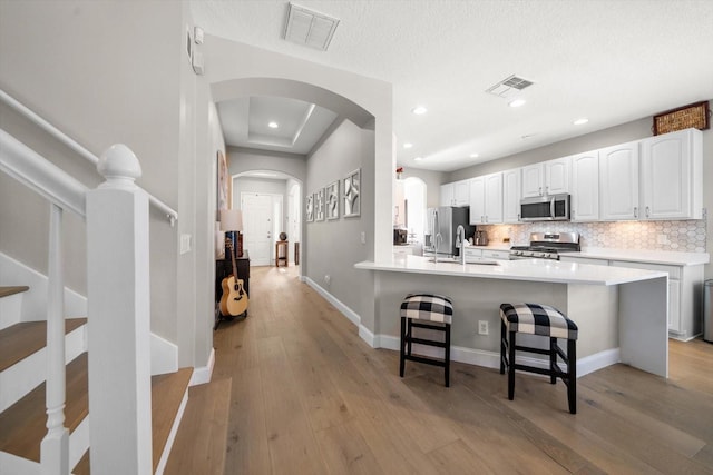 kitchen featuring white cabinetry, a kitchen bar, decorative backsplash, appliances with stainless steel finishes, and light wood-type flooring