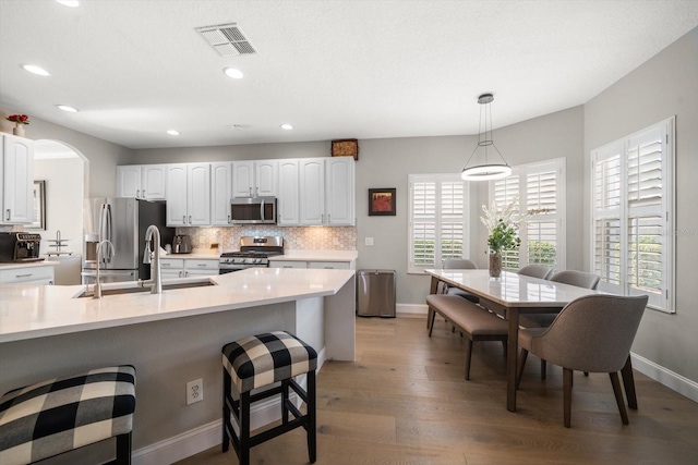 kitchen with appliances with stainless steel finishes, tasteful backsplash, decorative light fixtures, white cabinetry, and wood-type flooring