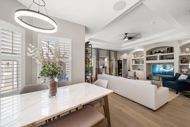 dining space featuring light wood-type flooring, a tray ceiling, built in features, and ceiling fan