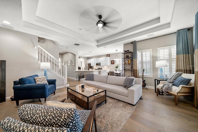 living room featuring ceiling fan, light hardwood / wood-style floors, and a raised ceiling