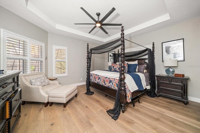 bedroom featuring a tray ceiling, ceiling fan, and light wood-type flooring