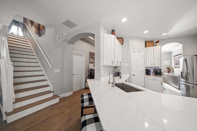 kitchen featuring white cabinetry, sink, light stone counters, and stainless steel refrigerator with ice dispenser