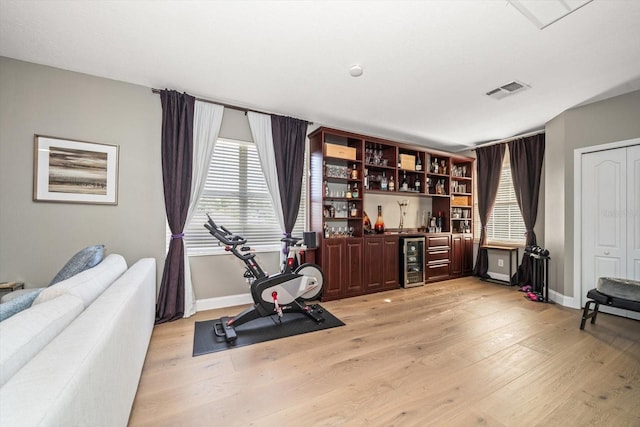 exercise room featuring bar area, wine cooler, and light wood-type flooring