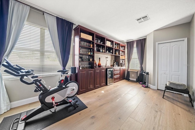 exercise room featuring a healthy amount of sunlight, light wood-type flooring, and wine cooler