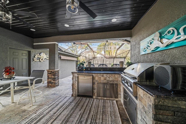 view of patio / terrace featuring glass enclosure, ceiling fan, area for grilling, and an outdoor kitchen