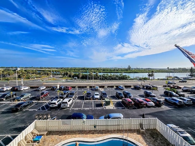 view of parking / parking lot with a water view and a fenced in pool