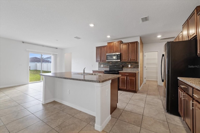 kitchen featuring sink, backsplash, a center island with sink, light tile patterned flooring, and black appliances