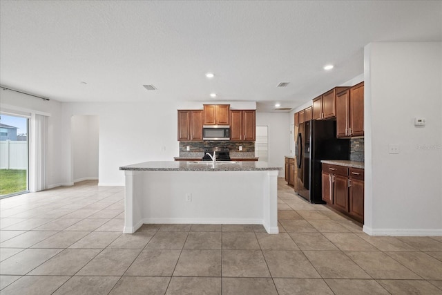 kitchen with sink, backsplash, a kitchen island with sink, black fridge with ice dispenser, and light tile patterned floors