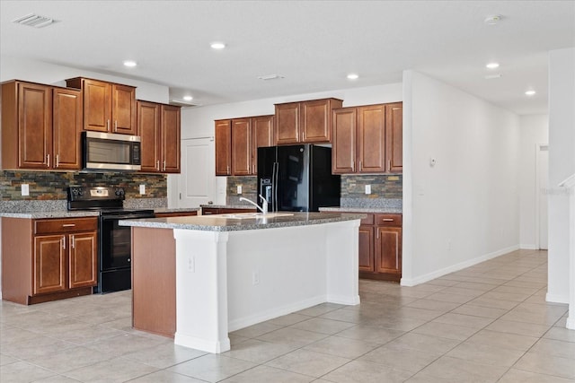 kitchen with tasteful backsplash, light stone counters, a kitchen island with sink, light tile patterned flooring, and black appliances