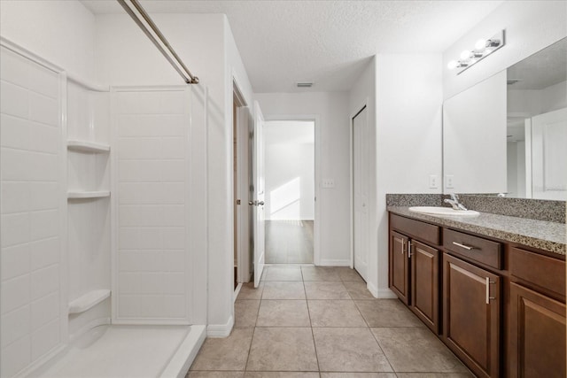 bathroom featuring tile patterned flooring, a textured ceiling, vanity, and walk in shower