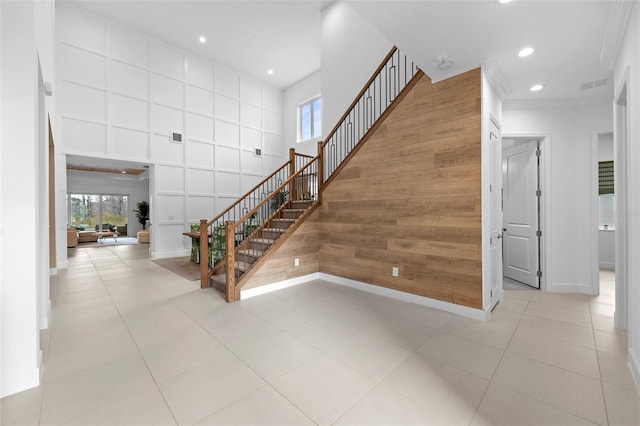 staircase featuring crown molding, a towering ceiling, tile patterned floors, and wood walls