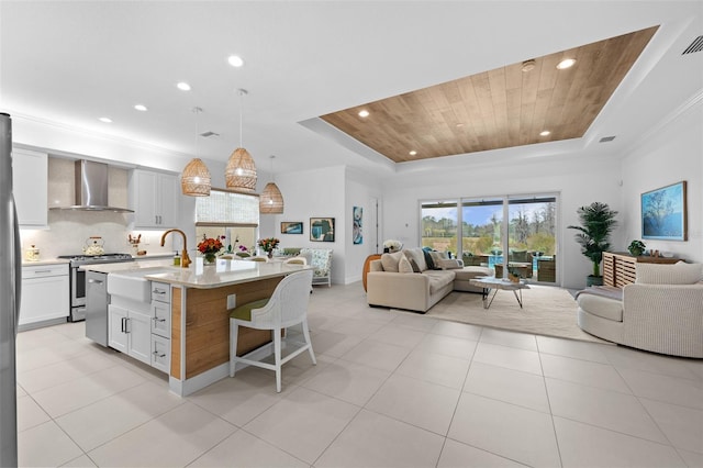 kitchen with a tray ceiling, white cabinets, and wall chimney exhaust hood