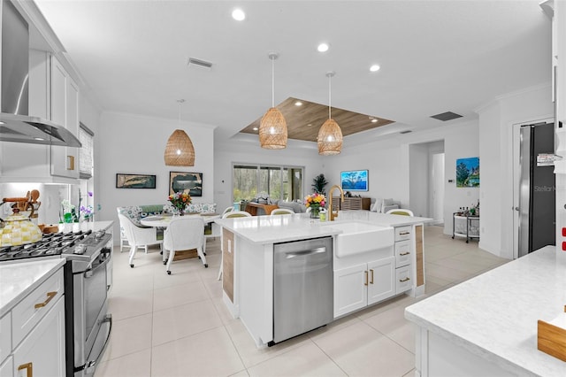 kitchen with white cabinetry, hanging light fixtures, a center island with sink, appliances with stainless steel finishes, and wall chimney range hood