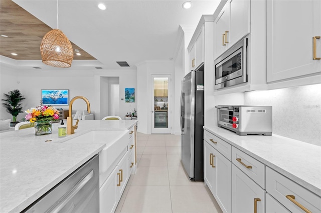 kitchen with light stone counters, appliances with stainless steel finishes, hanging light fixtures, and white cabinets