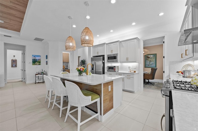 kitchen with light tile patterned floors, a breakfast bar area, stainless steel appliances, a center island with sink, and decorative light fixtures