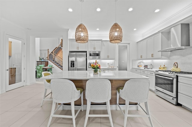 kitchen featuring a kitchen island, appliances with stainless steel finishes, pendant lighting, crown molding, and wall chimney range hood