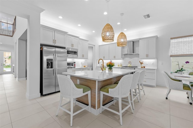 kitchen featuring pendant lighting, a breakfast bar, a kitchen island with sink, stainless steel appliances, and wall chimney exhaust hood