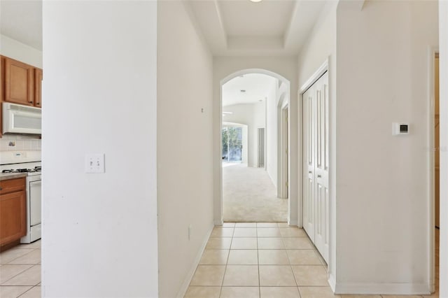 corridor featuring a tray ceiling and light tile patterned floors