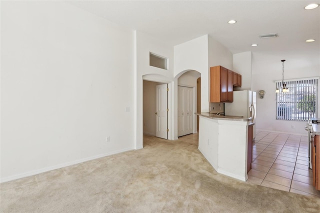 kitchen featuring hanging light fixtures, a notable chandelier, kitchen peninsula, a towering ceiling, and light colored carpet