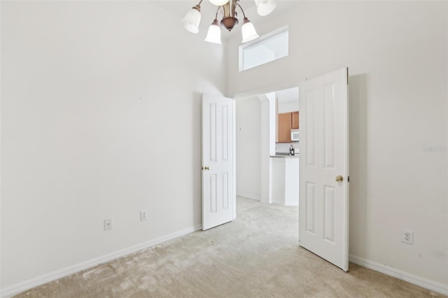 spare room featuring a chandelier, light carpet, and a towering ceiling