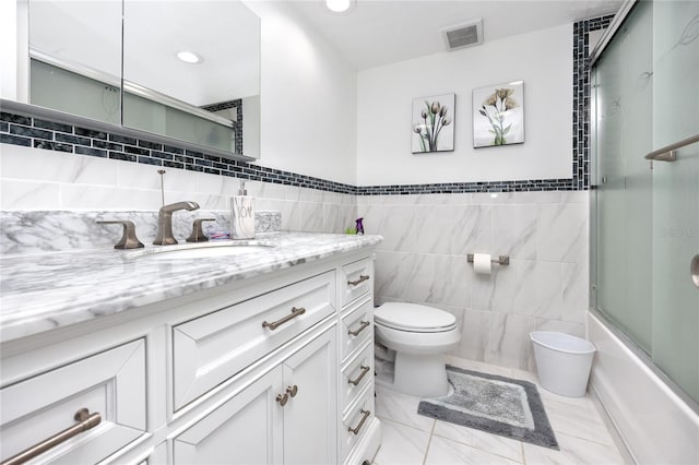 full bathroom featuring tile patterned flooring, toilet, shower / bath combination with glass door, vanity, and tile walls