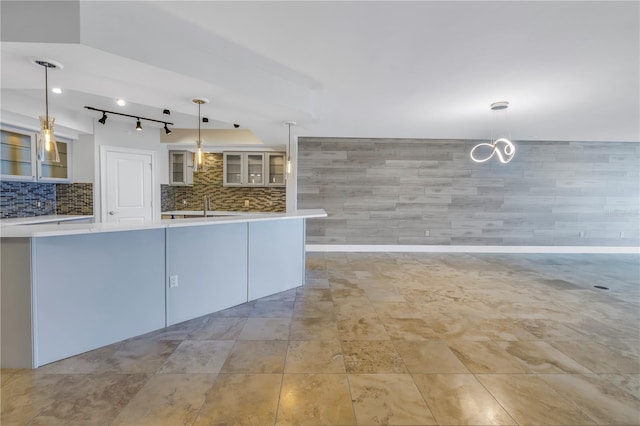 kitchen with glass insert cabinets, pendant lighting, light countertops, decorative backsplash, and a sink