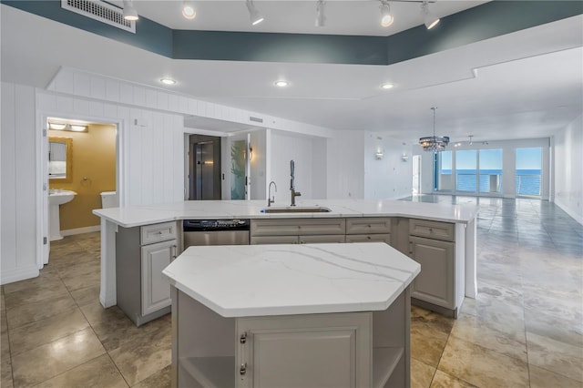 kitchen featuring gray cabinetry, sink, stainless steel dishwasher, a spacious island, and a water view