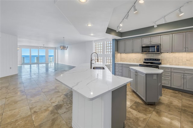 kitchen with a sink, stainless steel appliances, an island with sink, and gray cabinets