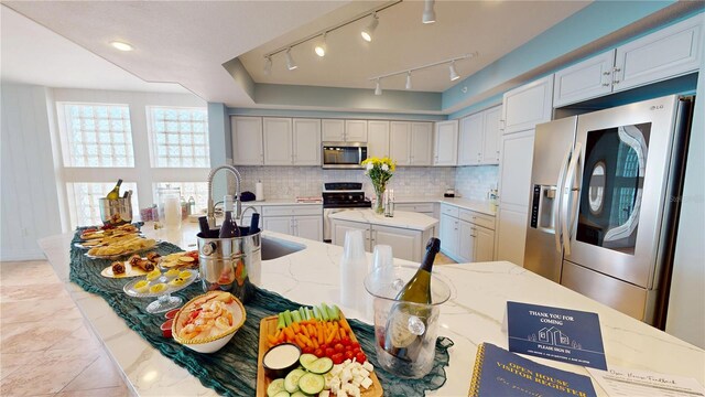 kitchen with light stone counters, backsplash, stainless steel appliances, and a sink