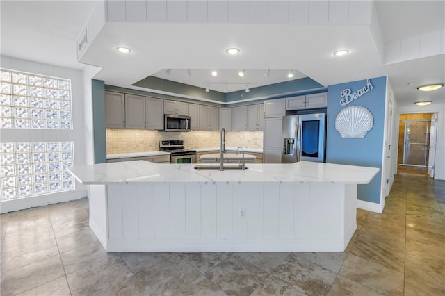 kitchen featuring light stone counters, decorative backsplash, a sink, stainless steel appliances, and gray cabinets
