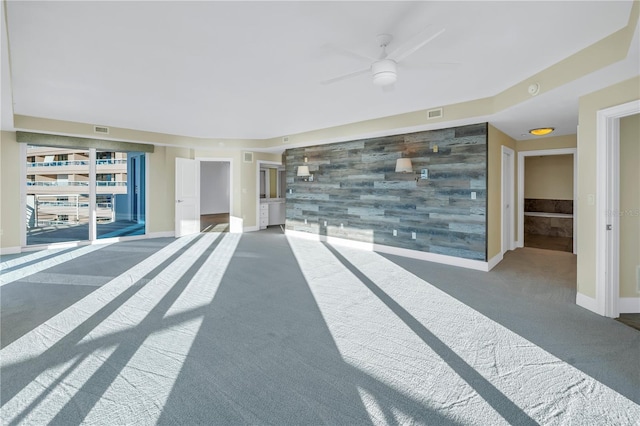 interior space with an accent wall, ceiling fan, baseboards, and carpet floors
